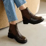 Bota corta de estilo chelsea con paneles laterales elásticos en contraste. Presenta una textura grabada tipo reptil en el cuero y una suela de plataforma dentada de goma negra.