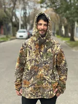 Canguro con capucha y cordones ajustables, confeccionado en tejido polar con estampado de camuflaje de hojas en tonos marrones, verdes y beige.