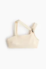 Top de bikini asimétrico de un solo hombro en color beige, con doble tirante y un detalle de aplique metálico dorado en la parte delantera.