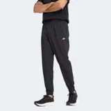 Pantalón tipo jogger New Balance Essentials Woven de color negro, confeccionado en tejido técnico con tecnología NB DRY que absorbe la humedad. Presenta una cintura elástica con cordón ajustable, bolsillos laterales funcionales y puños elásticos en los tobillos para un ajuste cómodo. Incluye el logotipo de la marca en contraste sobre la pierna izquierda.