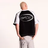 Camiseta de corte boxy fit con diseño de mangas raglán en color negro y cuerpo blanco. Presenta logo de la marca estampado en el pecho y etiqueta lateral decorativa.
