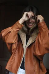 Campera oversize de cuero tostado con solapas y forro interno de corderito sintético azul marino, mangas anchas y detalles de costuras trenzadas.