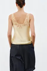 Top lencero de satén color beige con escote redondo y tirantes anchos, con aplicación de encaje a tono en el escote y los tirantes.