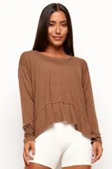 Remera de manga larga color marrón, confeccionada en una mezcla de viscosa, lino y elastano. Presenta un corte relajado con diseño asimétrico, destacando una costura horizontal en la parte frontal y bordes sin remate que le otorgan un estilo descontracturado.