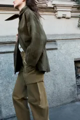 Chaqueta de algodón encerado con diseño de cuadros en tonos verde oliva, beige y líneas rojas. Presenta cuello solapa, cierre frontal con botones a presión metálicos, bolsillos de plastrón con solapa y un detalle de pañuelo desmontable sobre los hombros.