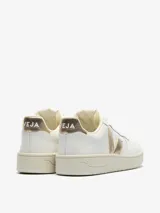Championes urbanos Veja modelo V-10, color blanco con detalles en dorado metalizado en el logo lateral y el talón. Presentan perforaciones en la puntera, cierre con cordones y suela de goma en tono crema.