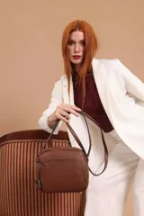 Bandolera de diseño compacto en color beige, confeccionada en material símil cuero con textura granulada. Cuenta con un bolsillo frontal con cierre y correa larga regulable.