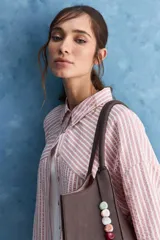 Camisa de calce relajado a rayas rosadas y blancas, con cuello camisero clásico y frente abotonado. Presenta recortes con cambio de dirección en las rayas y silueta amplia.