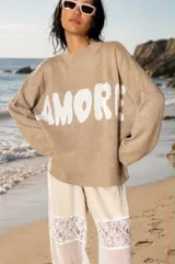 Sweater tejido de color beige con la palabra 'AMORE' estampada en grande en color blanco. Tiene cuello redondo y mangas largas y holgadas.