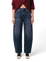 Jean de tiro alto con silueta barrel, caracterizado por su pierna amplia con una leve forma curva. Confeccionado en denim de color azul profundo con un sutil efecto lavado, presenta un diseño de cinco bolsillos y cierre frontal con botón y cremallera.