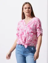 Blusa celeste con estampado blanco, de gasa, con cuello a la base y escote en V. Tiene abertura con botones, bolsillos delanteros y mangas 3/4 regulables con presilla y botón. El ruedo termina con un nudo.