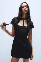 Vestido corto negro de cuello redondo con lazada, escote cuadrado y manga corta, con cierre en la espalda con cremallera oculta.