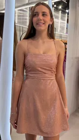 Vestido corto de lurex color rosado con acabado brillante, escote recto, tirantes finos regulables y falda con vuelo.