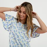 Blusa blanca con estampado de flores azules y verdes, cuello redondo con abertura en forma de gota y mangas cortas amplias.