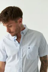 Camisa de manga corta con estampado de cuadros vichy en azul y blanco. Presenta cuello con botones, cierre frontal con botones y logo bordado en el pecho.