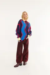 Sweater de punto con diseño geométrico en zigzag, combinando franjas en color marrón, rojo y negro. Presenta cuello redondo, mangas largas y un corte holgado.