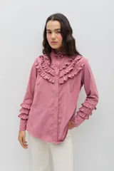 Camisa de manga larga en color rosado, con diseño de volados en cascada en el frente y en los puños. Presenta cuello alto con terminación suave y cierre frontal con botones.