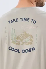 Remera gris oscuro de manga corta y cuello redondo, con un estampado gráfico en la espalda que incluye un paisaje de montaña y la leyenda "Take time to chill vibes cool down".