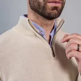 Buzo de punto color beige con cuello alto y medio cierre frontal.