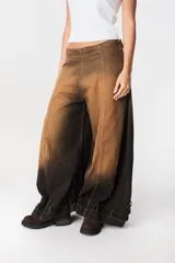 Jean de corte wide leg con efecto degradado en tonos marrón y negro. Presenta costuras verticales frontales y un diseño de puño ajustable en el bajo de la pierna.