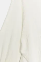 Blusa de cuello redondo y manga larga acabada en puño con frunces, detalle de aberturas en las mangas, frunces laterales y cierre trasero con abertura y botón.