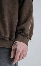 Buzo de cuello redondo color marrón oscuro con efecto desgastado (lavado óxido). Presenta costuras expuestas y detalles de pespunte ondulado en puños y ruedo. Tiene un calce oversize y crop.