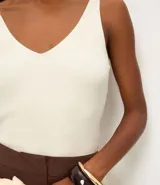 Blusa sin mangas de punto acanalado color crema, con escote en V y espalda descubierta. Confeccionada en una mezcla de viscosa y poliamida, presenta un ajuste al cuerpo y textura vertical en relieve.