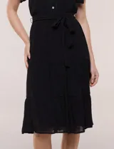 Vestido midi blanco de calce suelto y caída fluida, con escote en V, cuello a la base y apertura abotonada con detalle de puntilla. Cuenta con cintura elastizada con lazo para anudar a tono, mangas cortas con volados y falda con volantes escalonados.