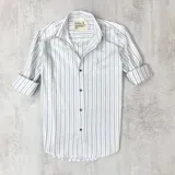 Camisa de algodón a rayas verticales celestes y grises claros, con cuello italiano y botones marrones.