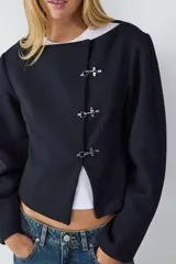 Campera corta de paño color negro, con escote redondo y manga larga. Presenta cierre frontal mediante tres ganchos metálicos decorativos. Diseño entallado con forro interior.