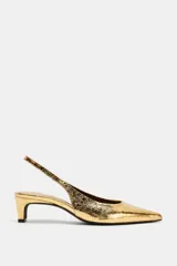 Zapatos tipo kitten heel destalonados, de color dorado con acabado metalizado texturizado, tacón bajo ancho y punta fina.