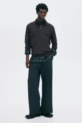 Buzo de punto fino color marrón oscuro, con cuello alto acanalado y medio cierre frontal. Presenta remates acanalados en puños y bajo.