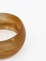 Pulsera tipo brazalete rígido de resina con efecto marmolado en tonos beige y tostado.