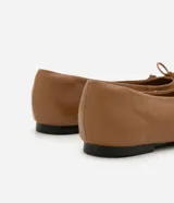 Zapatilla tipo bailarina Satinato confeccionada en cuero color tostado, con punta redondeada y detalle de mini lazo en la parte superior. Cuenta con suela plana de baja altura.