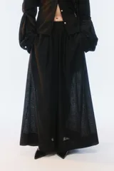Pantalón amplio de largo maxi, color negro, con piernas anchas, cintura elástica fruncida y diseño de tela liviana con textura calada transparente.