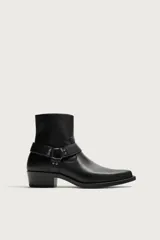 Bota de media caña color negro con detalle de arnés y hebilla lateral, punta perfilada y tacón bajo.