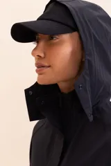 Campera negra de corte ancho y mangas raglán, confeccionada en tejido ligero y transpirable resistente al agua. Cuenta con capucha alta con cierre de cremallera y botones, mangas y barra ajustables, y bolsillo funcional en la parte delantera.