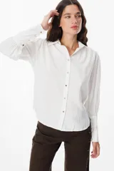 Camisa blanca de corte relajado, con cuello clásico, cierre frontal de botones y mangas largas amplias con puños ajustados.
