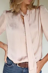 Camisa de seda color rosa, con cuello a la base y lazos frontales integrados. Presenta mangas con leve frunce en los hombros, puños elásticos y botones de nácar.