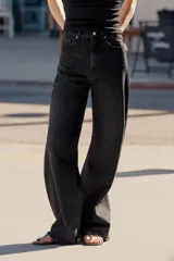 Jeans de mezclilla en color negro con efecto lavado, de tiro alto y cinco bolsillos, con perneras extra anchas y cierre frontal con cremallera y botón metálico.
