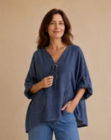 Blusa color azul jean con escote en V, cierre frontal con botones de madera y cordones ajustables, mangas largas con presilla y bolsillos delanteros con detalles desflecar.