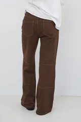 Pantalón de corte recto confeccionado en gamuza color marrón, con costuras a la vista en tono contrastante y diseño de paneles horizontales en las piernas.