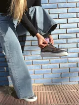 Zapatillas deportivas de cuero color peltre, con cordones negros y suela de goma blanca.