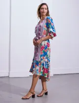 Vestido midi con estampado floral en tonos azules, rojos y blancos. Tiene escote en V, mangas 3/4 con puños fruncidos, cintura elastizada con lazo de ajuste y falda con volantes.