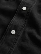 Camisa de jean de corte clásico en color azul oscuro, con cierre frontal de botones, cuello camisero y dos bolsillos frontales con solapa y botón.