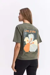 Remera de algodón color verde oliva, con corte relajado y manga corta. Presenta una estampa gráfica grande en la espalda con motivos florales abstractos y texto.
