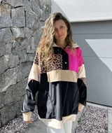 Buzo de estilo canguro con diseño color block que combina paneles en negro, fucsia, beige y un estampado de leopardo. Presenta cuello con cierre de botones a presión y un bolsillo frontal tipo canguro.
