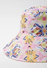 Gorro tipo bucket hat estampado con flores y hojas en tonos verde y celeste sobre fondo blanco. Es reversible.