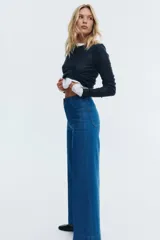 Pantalón de jean de tiro alto, color azul medio, con pierna ancha y corte ajustado en la cadera. Presenta bolsillos de parche tanto en la parte delantera como en la trasera.