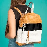 Mochila de cuero vacuno color camel, con detalles en negro y blanco. Tiene dos bolsillos frontales con cierre, correas ajustables, interior forrado con bolsillo con cierre y bolsillo para celular.